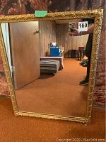 Full view of rectangular mirror with ornate gold frame against a wood wall background.