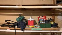 Wide shelf view showing cooler, camp stove in box, green tent bag, black bike rack, first aid kit, cooking pot, and some packaged camping accessories such as rain poncho and matches.