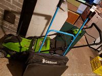 Overview of Greenworks electric mower and Gardena hand mower side by side on the floor showing side and handle details.