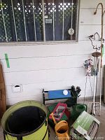 Wide view of assorted garden supplies arranged on patio including garden bench with tool belt, watering cans, lantern hanger, wind chime and fold-up bins with gloves.