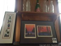 Framed Roy H. Vickers art prints 'Ya-a' and 'Tsi-i' and four glass vintage soda bottles on a wooden shelf, including a green Hi-Spot bottle.