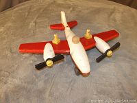 Angle view of the vintage 1950s Playskool airplane toy showing the red wings, white fuselage, black propellers, yellow cockpit and wooden knobs as pilots or passengers. The toy shows some age wear.