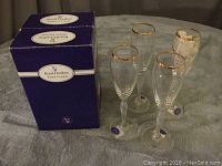 Photo of four champagne flutes and two blue Royal Doulton Finest Crystal boxes on a grey surface, showing packaging and multiple items.