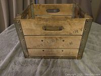 Front side of wooden milk crate showing faded stenciled words 'ROYAL DAIRY' with metal corner brackets.
