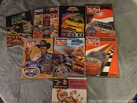 Collection of NASCAR books and magazines laid out on a fabric surface showing colorful covers with race cars, Pepsi logos, and 1960s football pictorial.