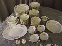 Full view of stacked plates, cups, gravy dish, large serving bowl, platter, and shakers on a surface.