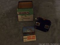 View of the stereoscope viewer, original box, and reel list booklet arranged on a surface