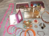 Photo of assortment of costume jewelry laid out including necklaces, bangles, brooches, earrings, and compact mirror