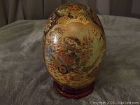 Full view of Satsuma hand painted egg on wooden stand showing intricate floral and bird motifs and gold detailing.