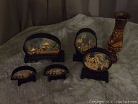 Full view of all five Chinese cork art pieces and the wooden vase on a textured surface.