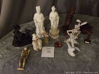 Group of assorted figurines and decor items on gray fabric surface, including animals, human figures, and small decorative pieces