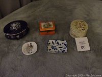 Photo shows all five trinket boxes and the pin dish arranged on a grey fabric.