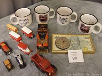 Overview of the mugs, diecast vehicles, repair kit box, and framed clock on a gray cloth.