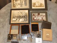 Overview of vintage mounted photos, wooden photo holders, and several glass plate photographs laid out on cloth surface.