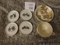 View of four pin dishes with vintage car illustrations and the cup and saucer cup. Pin dishes are round with gold rims, designs in center.