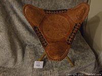 Front view of the triangular leather saddle stool showing embossed design and leather lacing on the edges.