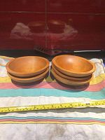 Five wooden salad bowls side by side showing overall shape and warm wood tone, laid out on colorful striped cloth with tape measure for scale.
