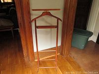 Full front view of vintage wooden clothing valet butler with hanger and lower bar on wooden floor