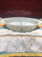 Front angle view of a white oval divided vegetable dish with gold starburst decoration on the side, sitting on a cloth.