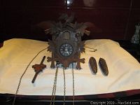 Front view of wooden cuckoo clock with chains, weights, and pendulum laid out in front of it on a cloth.