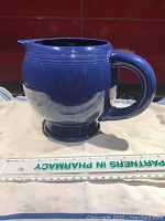 Side view of cobalt blue ceramic pitcher with ice lip and handle, placed next to a ruler for size reference.