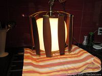 Front-on view of pendant light showing walnut slats around white glass globe and brass frame