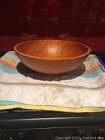 Large wooden serving bowl on a striped cloth, showing full side profile with gentle curve and rounded lip.