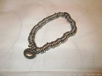 Full view of the silver multi-ringed bracelet laid on white surface, showing the band made of many stacked rings and the attached charm.