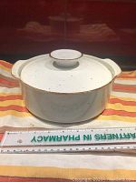 Front view of white ceramic casserole dish with lid on, placed on striped fabric with a ruler for scale.