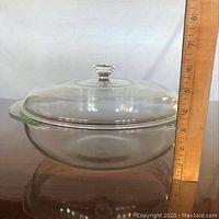 Side view showing the full height of the clear Pyrex round casserole dish with lid, next to a wooden ruler measuring about 4.5 inches tall.