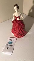 Full view of porcelain figurine of a woman in red dress with auction number tag