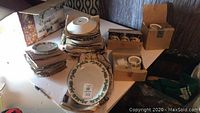 Photo showing stacks of plates, bowls, cups, and saucers with Christmas holly pattern on a table.
