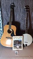 Photo of Ariana acoustic guitar and Widman banjo side by side with banjo instruction book in front.