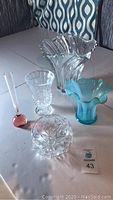 Photo of 5 assorted vases showing clear and blue glass pieces including the large scalloped rim vase, blue ribbed vase, cut glass bowl-shaped vase, smaller ribbed vase, and small pink narrow neck vase.