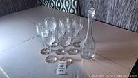 Front view of six crystal wine glasses and crystal decanter on table with sale tag visible.