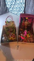 Two boxes of toys: one box contains wooden activity cube, vintage Fisher Price push toy, plastic fake fruit; the other box contains vintage Barbie case with Barbie dolls and pieces.