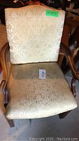 Front view of the vintage occasional chair showing the patterned beige upholstery and wooden arms and legs.