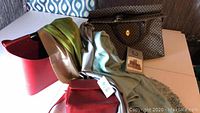Red leather-look magazine holder, red purse, four scarves and Alfred Sung overnight doctor's bag with tag all displayed on a table.