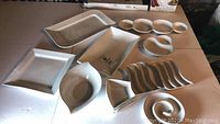 Photo of white ceramic serving ware assortment including rectangular platters, oval bowls, small square dishes, wavy edge trays, and spiral plates on a table