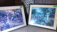 Two framed art prints side by side showing garden scenes with women and children. Each frame has size stickers 33x39 and 31x36 inches.