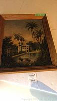 Full view of framed antique oil painting of palm trees and a large house with pond.