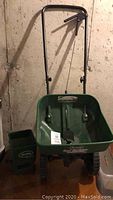 Full view of one Scotts Turf Builder seed spreader with handle and wheels in a basement setting