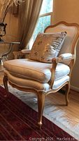 Front-right angle view of chair showing carved wood frame, scrolled arms, cream upholstery