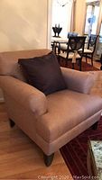 Full view of the brown upholstered armchair with black pillow showing armrests and seat cushion.