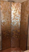Front view of the three-panel room screen showing gold or bronze embossed metal floral pattern on wood panels.