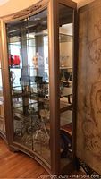 Front and side views of wooden framed glass display cabinet showing carved detail and glass shelving inside with displayed decorative items.