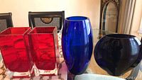 Four glass vases on table: two red square-shaped vases and two blue tall vases.