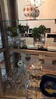 Glass shelf showing two small clear glass pots containing faux plants and glass platter below