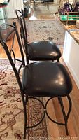 Side profile showing two black vinyl seat cushion metal frame bar chairs with decorative back and footrests.