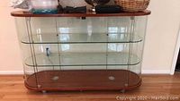 Full front view of glass display cabinet with wooden top and bottom, containing two glass shelves and visible lighting, against wall.